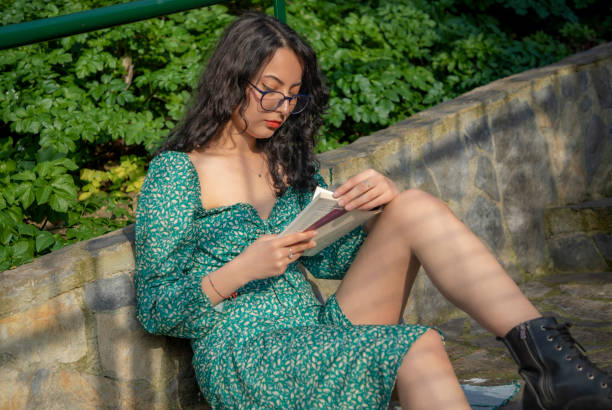 Young woman with brunette glasses reading a book outside