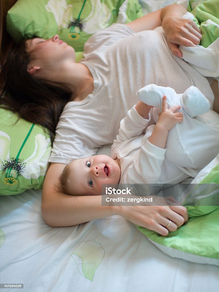 Baby with mom Awake baby with sleeping mom in a bed Baby - Human Age Stock Photo