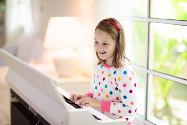 Child playing piano. Kids play music. Classical education for children. Art lesson. Little girl at white digital keyboard. Instrument for young student. Music class in school or at home.