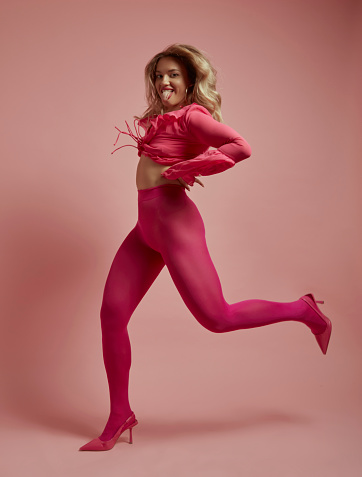 Beautiful blonde woman jumping in front of pink background.