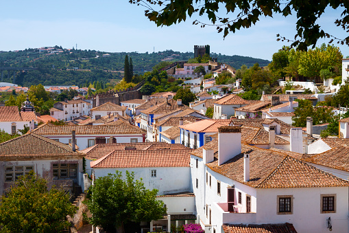 View over the medieval walled town of Obidos in Portugal on a bright summers day with a blue sky overhead and hills in the background.