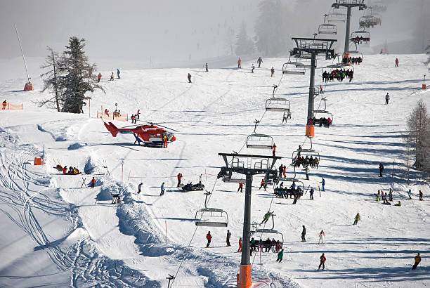 Popular slope at Nassfeld ski resort with landed rescue helicopter Crowded slope under a ski lift at Nassfeld ski resort. Rescue helicopter has landed on the slope. Medics are helping injured skier. Snowmobiling stock pictures, royalty-free photos & images