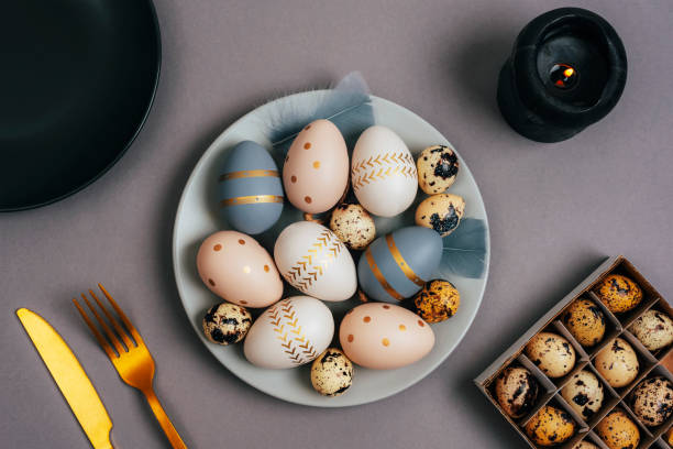 istock Gray plate with painted Easter eggs, candle and fork and knife on a gray background. Easter table setting. Top view, flat lay 1470353606