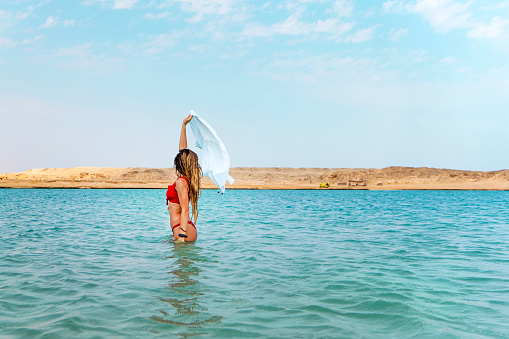 A young beautiful woman walks on the turquoise water of the red sea. Sharm el Sheikh, Egypt. The concept of a summer holiday by the sea.