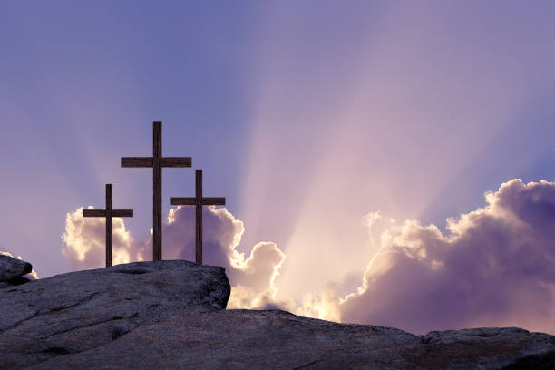 Three crosses on a hill at sunrise symbolize the Crucifixion of Christ as the sun rises in the distance.
