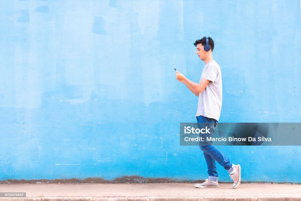 Music streaming service Young man wearing wireless headphones and listening to streaming music via app on his smartphone, while walking on the street sidewalk. Headset Stock Photo