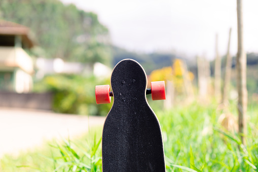 Isolated top of a longboard with red wheels standing outdoors.