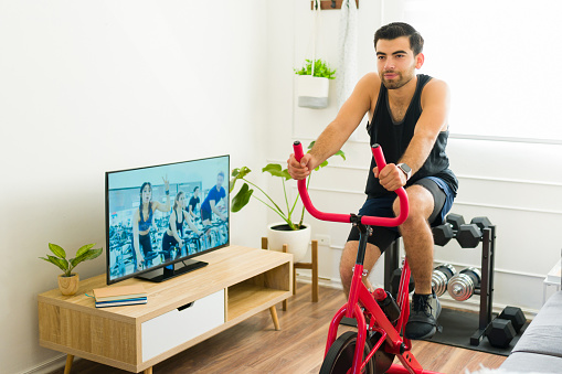 Determined man with a fitness motivation riding his stationary bicycle and doing cardio exercise at home