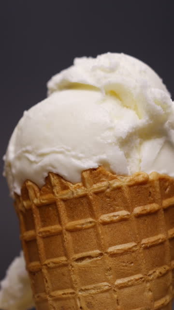 Vanilla ice cream scoop in cone on pink background.