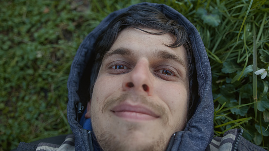 Smiling Young Man Lying on the Grass in the Middle of Nature Looking at the Camera, Close-up Shot