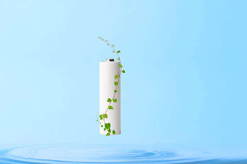 Rechargeable battery and green leaves floating in mid-air from the water surface, against light blue background with copy space. 
Concept of clean energy and recycling.