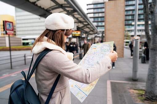 Young tourist Woman stand reading bus map at bus stop, Japan