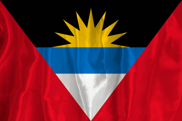 le drapeau d’antigua sur fond de soie est un grand symbole national. texture du tissu le symbole officiel de l’état du pays. arrière-plan du drapeau - antiguan flag photos et images de collection