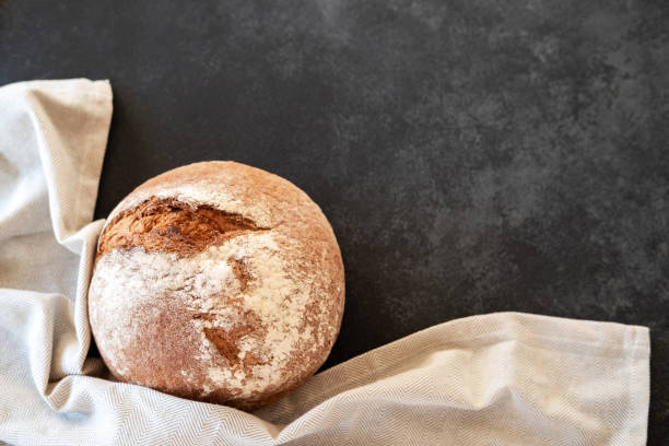 istock Freshly baked bread loaves with kitchen towel on black background. 1470409343