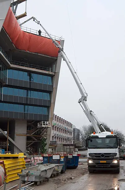 A concrete truck is pumping concrete to the 6th floor of a highrise building on a rainy day