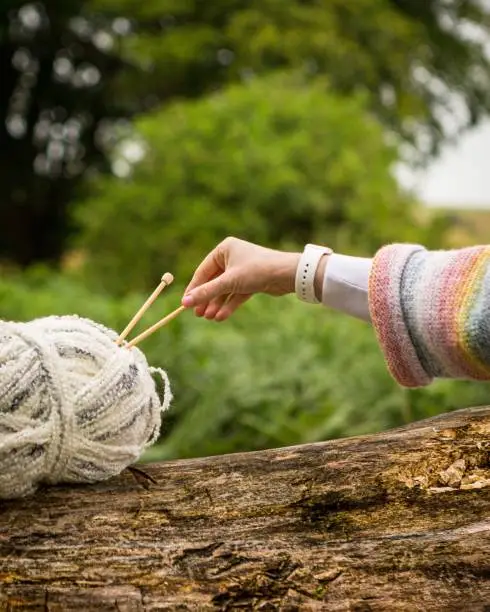 A woman reaching to take a knitting needle  while balancing a wooden skewer in her hand