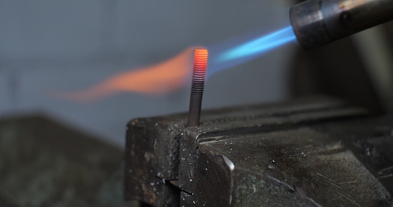 Close-up. A blowtorch heated a piece of metal rod. The metal burns bright red when heated by a blowtorch. A man soldering metal with a blowtorch..