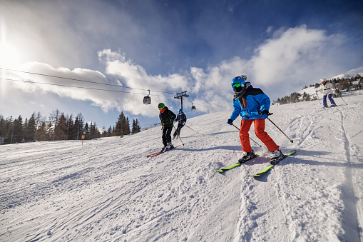 Young active woman skiing in mountains. Female skier kid with safety helmet, goggles and poles enjoying sunny winter day in Swiss Alps. Ski race for adults. Winter and snow sport in alpine resort.