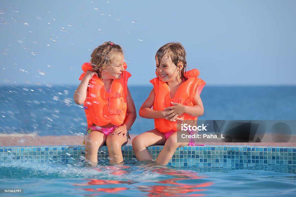 Due bambine in vita-giacche seduto sulla terrazza della piscina - Foto stock royalty-free di Bambino