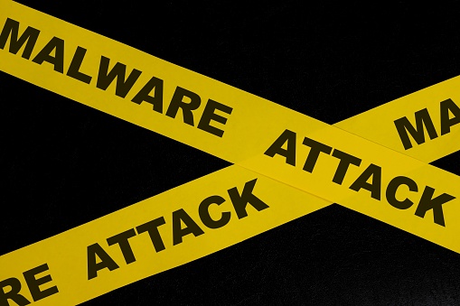 Malware cybercrime alert, caution and warning concept. Yellow barricade tape with word in dark black background.