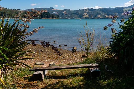 Uitzicht over Broad Bay, Otago, Dunedin. Op de voorgrond is een bankje waar waaraf je uitkijkt over het blauwe water van de baai bij Dunedin.