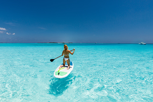 Rear view of a woman stand up paddling during summer day at sea. Copy space.