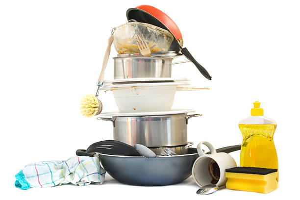 A stack of dirty dishes, pots, and pans by soap and rags