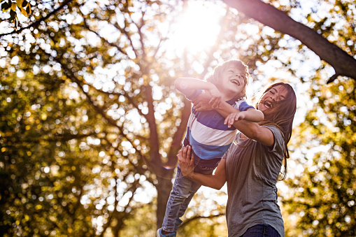 Low angle view of happy mother having fun while playing with her small boy during springtime in nature. Copy space. Focus is on boy.