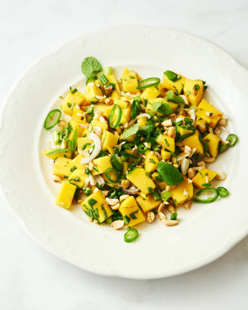 istock Thai mango salad in the white plate on white background. Salad from mango with peanuts, chili and fish sauce decorated with mint leaves. 1470431000