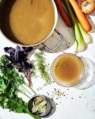 Vegetable stock in glass bowl. Ingredients of stock on the background. High quality photo