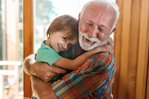 Cute little boy enjoying in a hug with his senior grandfather at home.