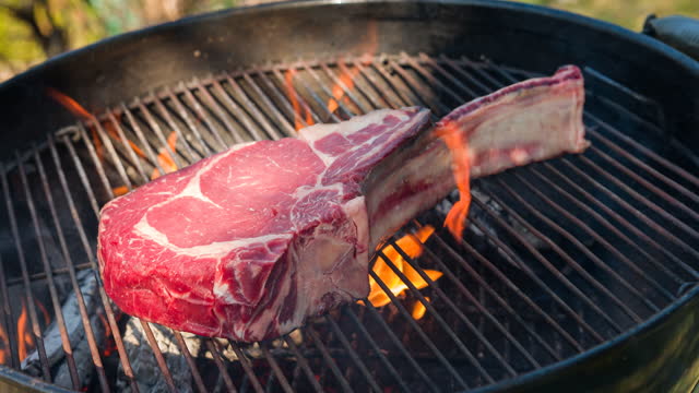 Tomahawk steak being grilled over open flames on barbecue grill