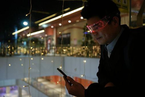A man wearing smart glasses uses his mobile phone at night