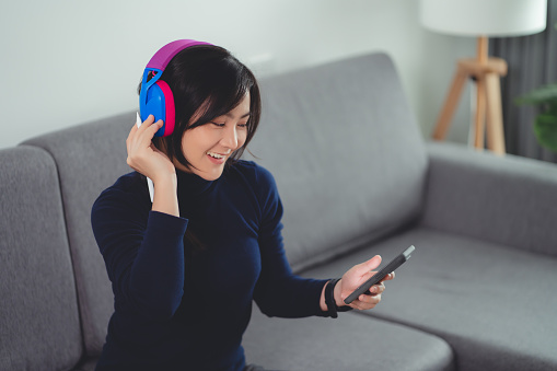 Happy woman using smart phone with headphones listening to music enjoy and dancing sitting at home.