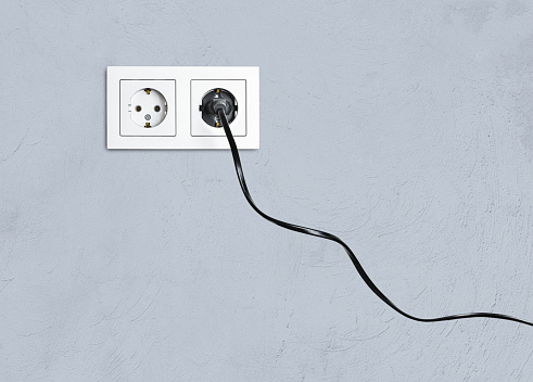 electrical socket and plug in it, against the background of a gray wall