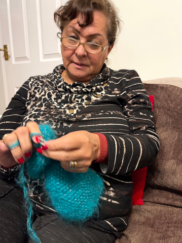 Senior Hispanic woman at home making crochet items sitting on sofa