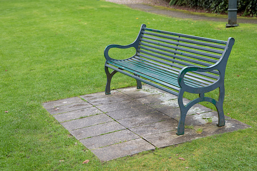 A green bench made of wood and concrete photographed on a sunny spring day in Nyon, Switzerland. In this photo you can also see some grass, trees, buildings and blue sky. Color image.