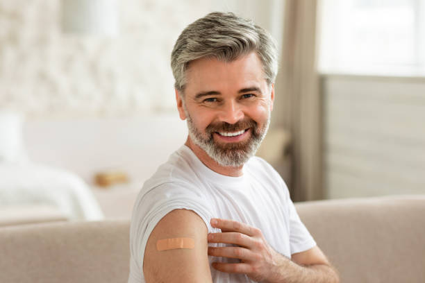 istock Joyful Vaccinated Man Showing Arm With Adhesive Bandage Sitting Indoors 1470440668