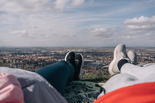 Young couple of hikers lying down to rest on a green blanket at the top of the mountain.
