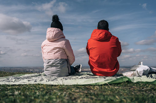 Young couple of hikers sitting on their backs to rest on a green shawl at the top of the mountain.