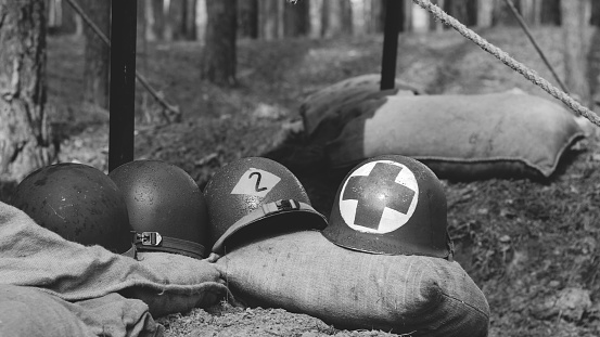 WWII American Metal Helmets Of United States Army Infantry Soldier At World War II. Helmets Near Camping Tent In Forest Camp. Black And White Colors.