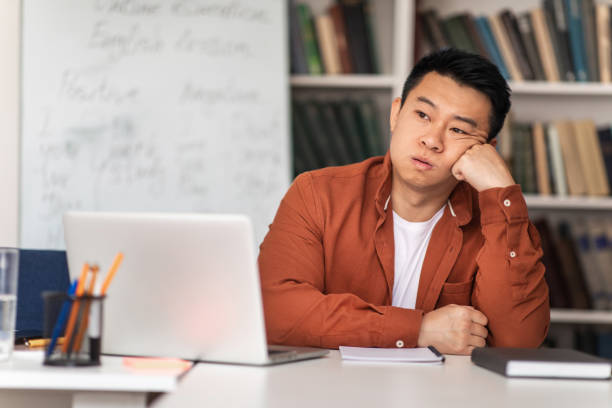 Unhappy Asian Teacher Sitting At Workplace Having Problem In Classroom