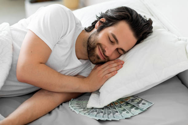 istock Smiling bearded guy sleeping with cash under his pillow 1470444695