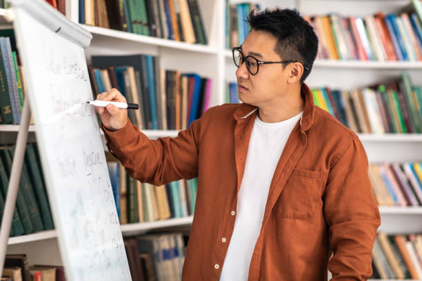 istock Asian Teacher Man Having Class Writing On Whiteboard In Classroom 1470444880
