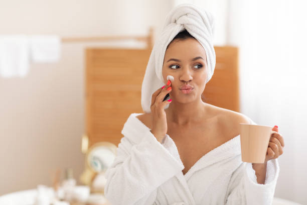 istock Playful Woman Applying Moisturizer On Face Holding Coffee In Bathroom 1470444983