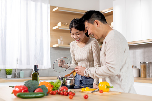 Cheerful japanese family middle aged husband and young wife enjoying cooking together at home, happy asian man and woman standing next to stove, preparing healthy dinner, copy space
