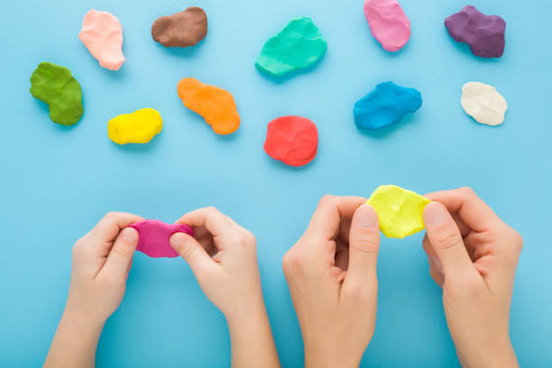 istock Mother and child hands holding and kneading modeling clay on blue table background. Pastel color. Closeup. Point of view shot. Preparing material for making different colorful shapes. Top down view. 1470445343