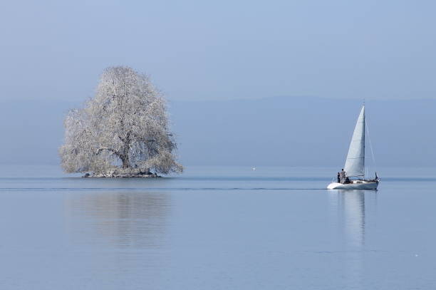 The sailboat sails on the lake in front of a mast in the middle of the lake