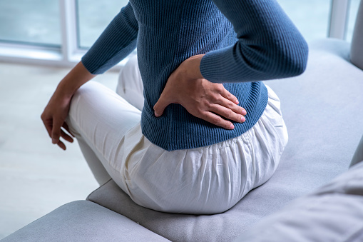 Woman suffering from back ache on the sofa. Female with back pain at home