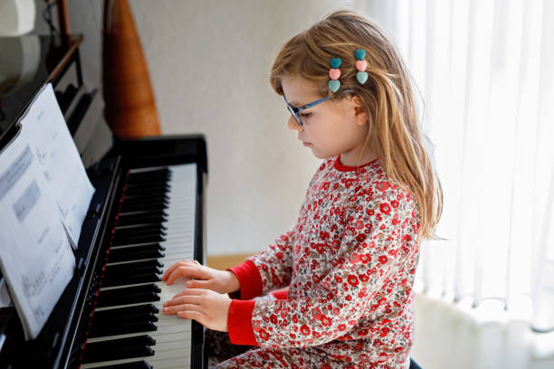 居間でピアノを弾く小さな幸せな女の子。眼鏡をかけたかわいい未就学児が楽器の演奏を楽しんでいる。 - piano keyboard instrument one person piano key ストックフォトと画像